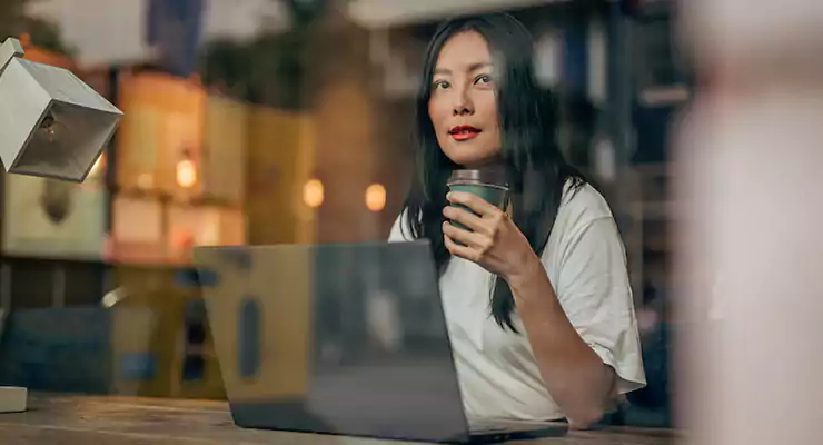 mulher nova pensativa tomando seu café enquanto trabalho no seu computador